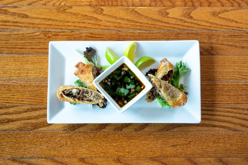 Crispy fried egg rolls with a savory filling, served with a dipping sauce and lime wedges.