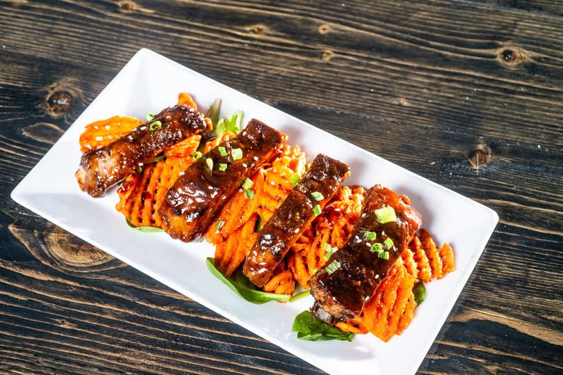 Glazed ribs with sesame seeds and green onions, served on waffle-cut sweet potatoes and spinach.