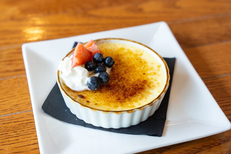 Crème brûlée in a white ramekin, topped with whipped cream, blueberries, and sliced strawberries.