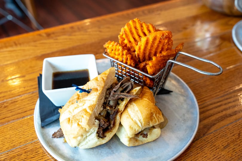 French dip sandwich with waffle fries and au jus on a light blue plate.
